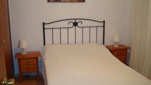 A bedroom with a single bed, two bedside tables with lamps, a wooden nightstand, and a painting on the wall. - 3 Bed Flat - Sleeps 5 - Parking - Wifi (Tarifa)