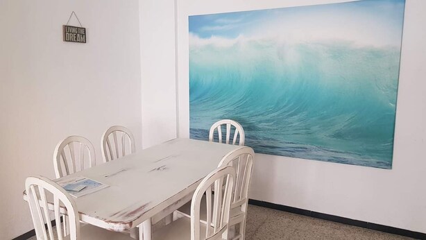 A dining area with a white table and chairs, a large wave painting on the wall, and a 'Living the Dream' sign. - 3 Bed Flat - Sleeps 5 - Parking - Wifi (Tarifa)