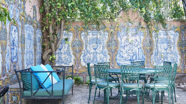 Eine Terrasse mit einem grünen Metalltisch und -stühlen, einer blauen gepolsterten Couch und einer dekorativen Wand mit kunstvollen Fliesenmustern.