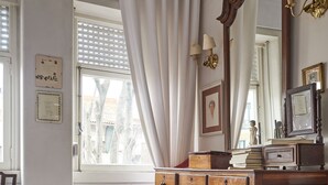 Ein Zimmer mit einem Holzkoffer, einem Stuhl, einem gemusterten Teppich und einem großen Spiegel.