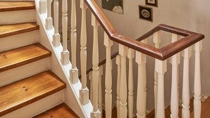 Eine Treppe mit weißen Balustern und Holzhandläufen, die zu einer Zwischenebene mit gerahmten Bildern an den Wänden führt.