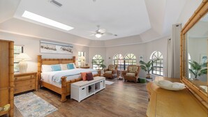 Een ruime slaapkamer met een groot bed, een plafondventilator, een houten dressoir en een grote spiegel.