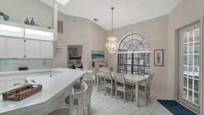 Een moderne keuken met witte kasten, een groot eiland en een eethoek met witte stoelen.