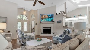 Een ruime woonkamer met een open haard, comfortabele zithoek en een grote televisie erboven.