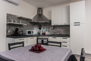 A modern kitchen with white cabinets, a stainless steel range hood, a microwave, and a kettle on the counter.
