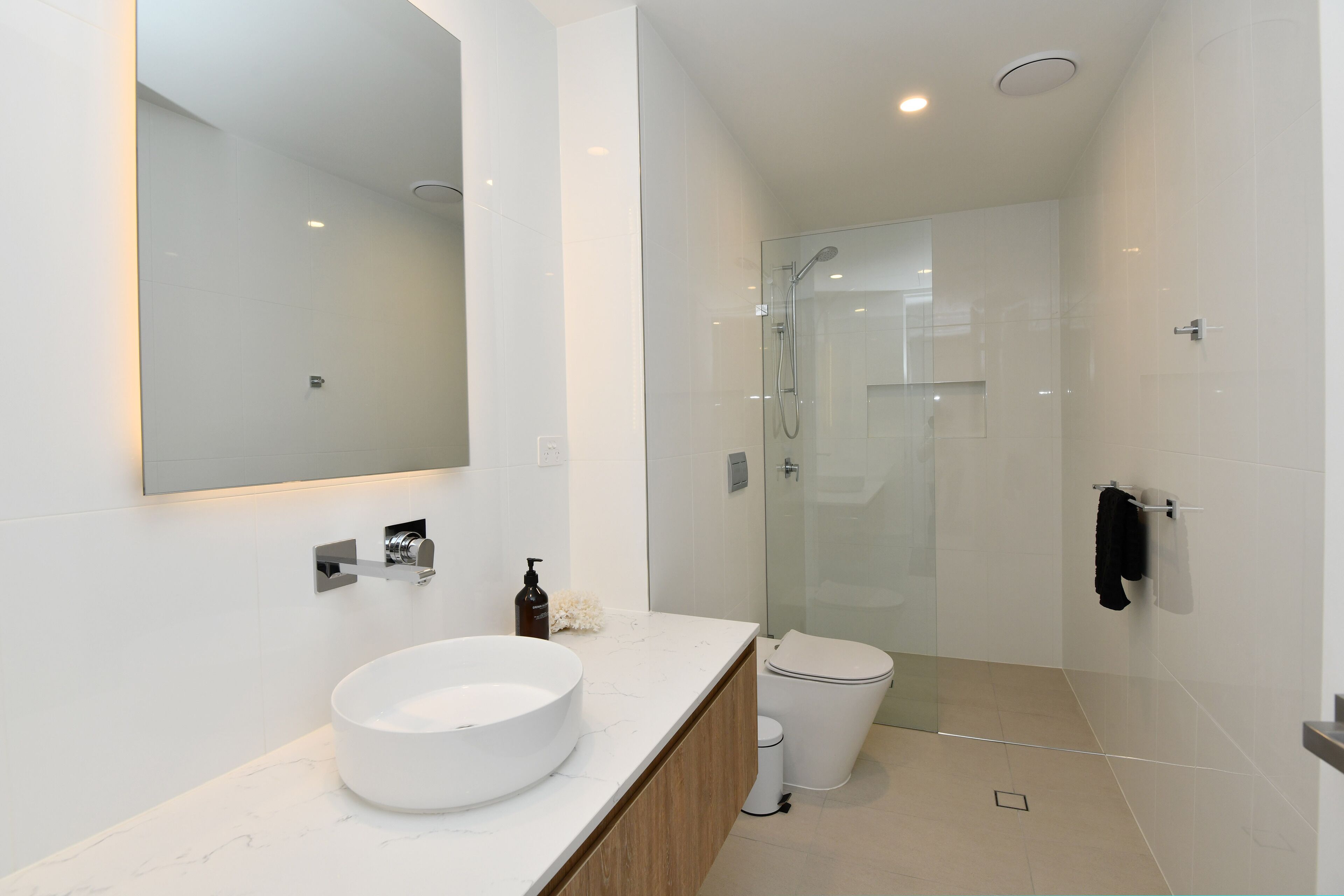 A modern bathroom with a large mirror, a round sink, a glass shower enclosure, and a toilet.