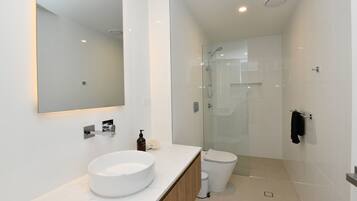 A modern bathroom with a large mirror, a round sink, a glass shower enclosure, and a toilet.
