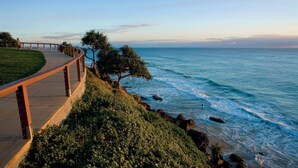 A coastal walkway with a wooden railing, leading to a beach with waves crashing onto the shore. - X Kirra Apartments (Coolangatta)