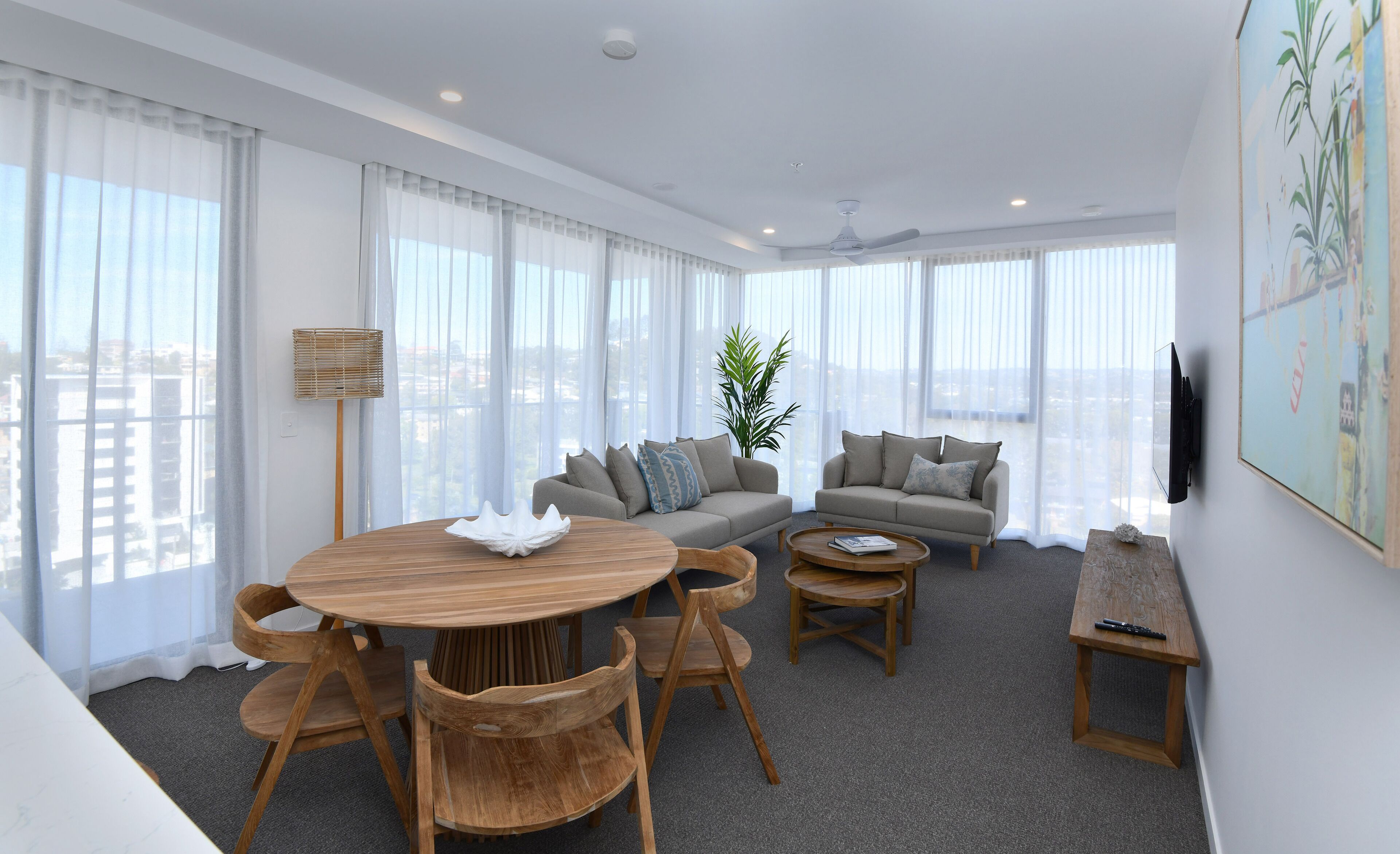 Una sala de estar moderna con una mesa redonda de madera, dos sofás y un amplio ventanal con vistas a la ciudad.