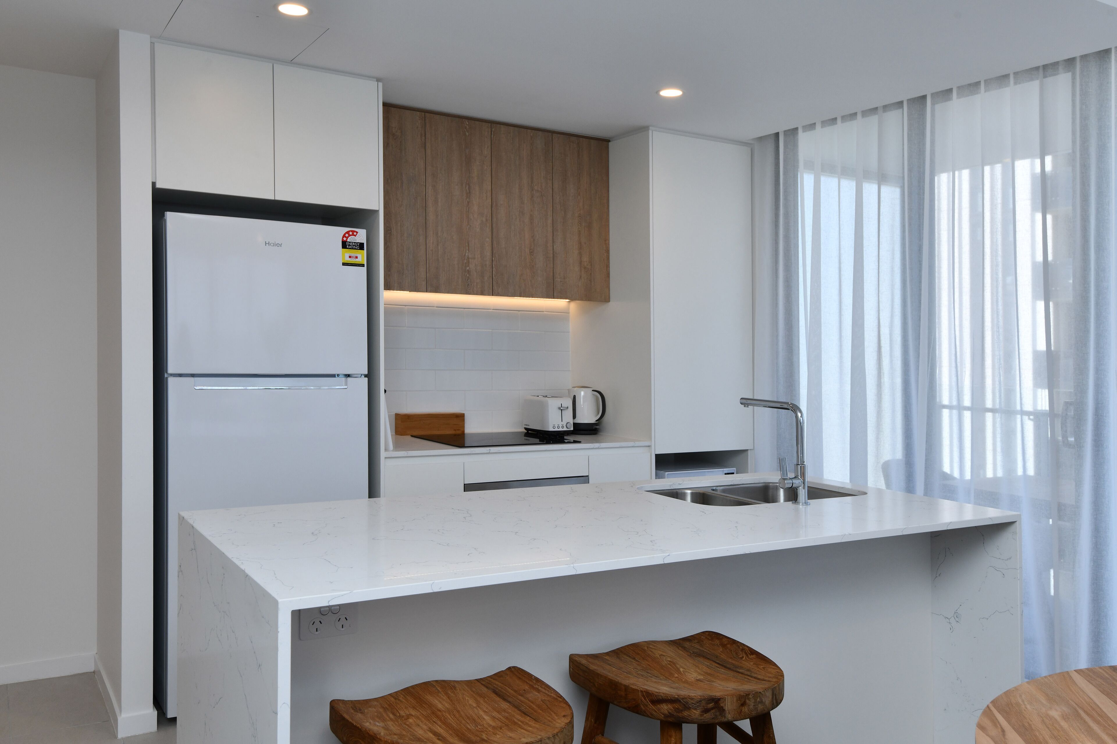 Una cocina moderna con encimera blanca, armarios de madera, horno empotrado y pileta.