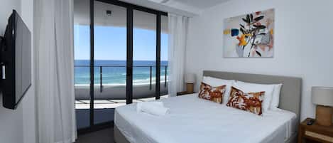 A hotel room with a bed, a TV, a ceiling fan, a painting, and a view of the ocean.
