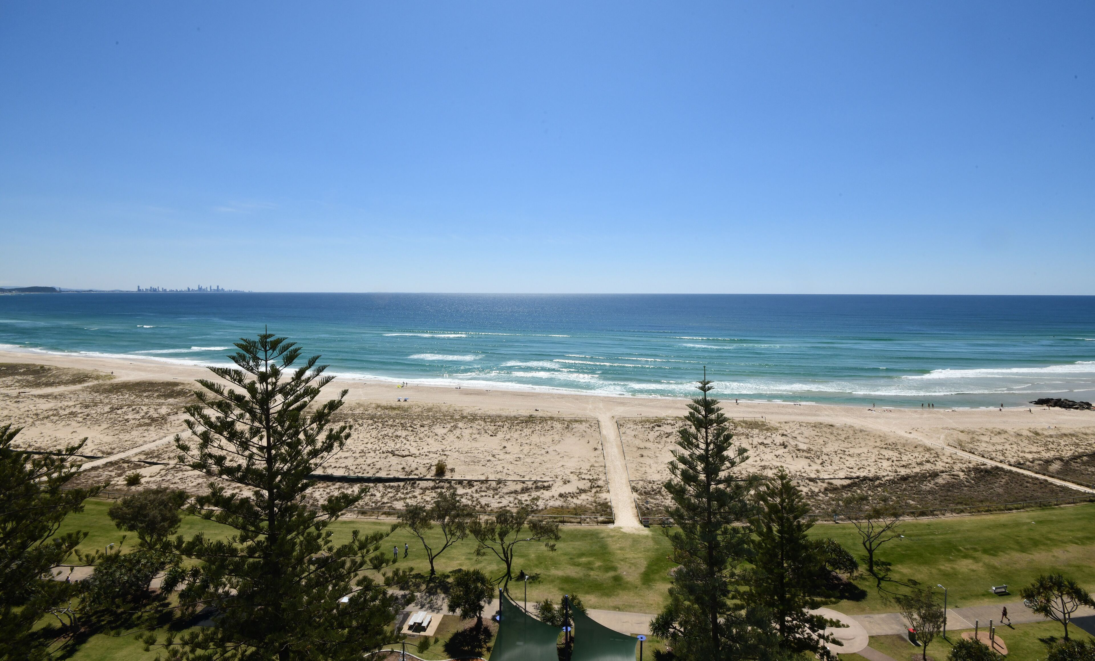 Une vue sur la plage, avec un ciel dégagé, une plage de sable et, au loin, les contours d’une ville.