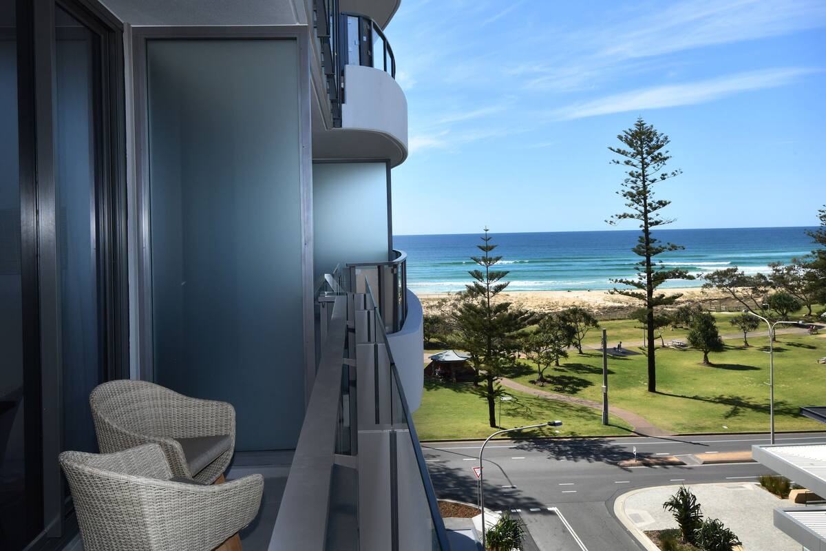 A balcony with a wicker chair, a glass door, and a view of the beach and ocean.
