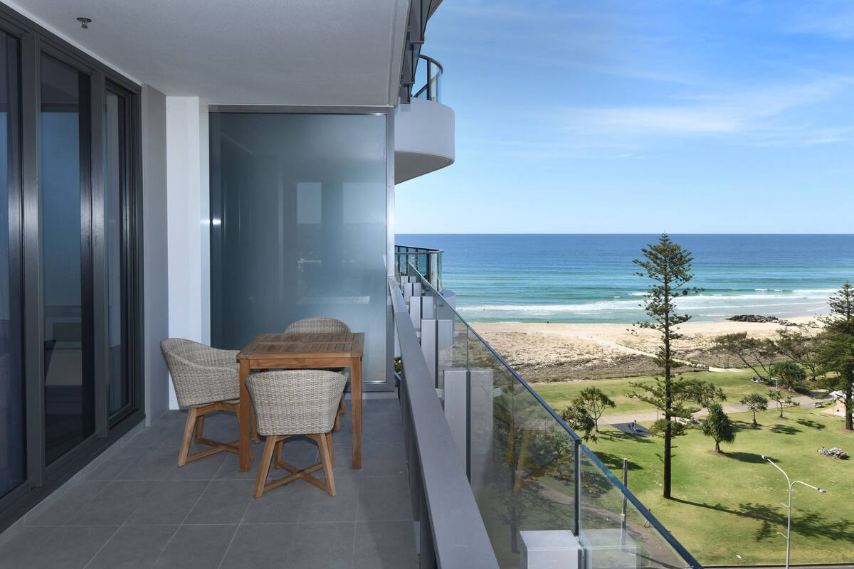 A balcony with a table and chairs overlooking a beach.