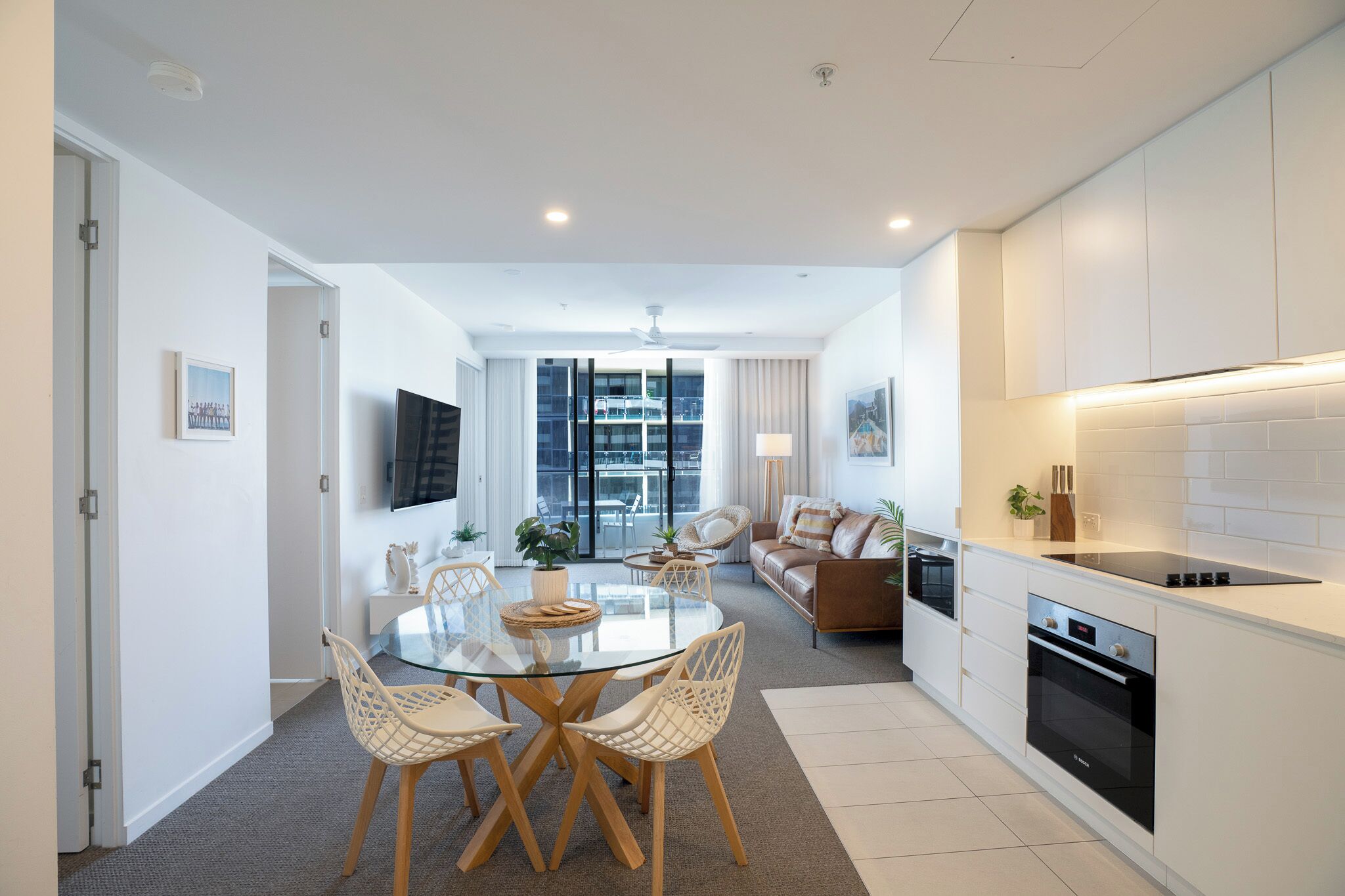 A modern kitchen with white cabinets, a black oven, and a glass dining table with chairs.