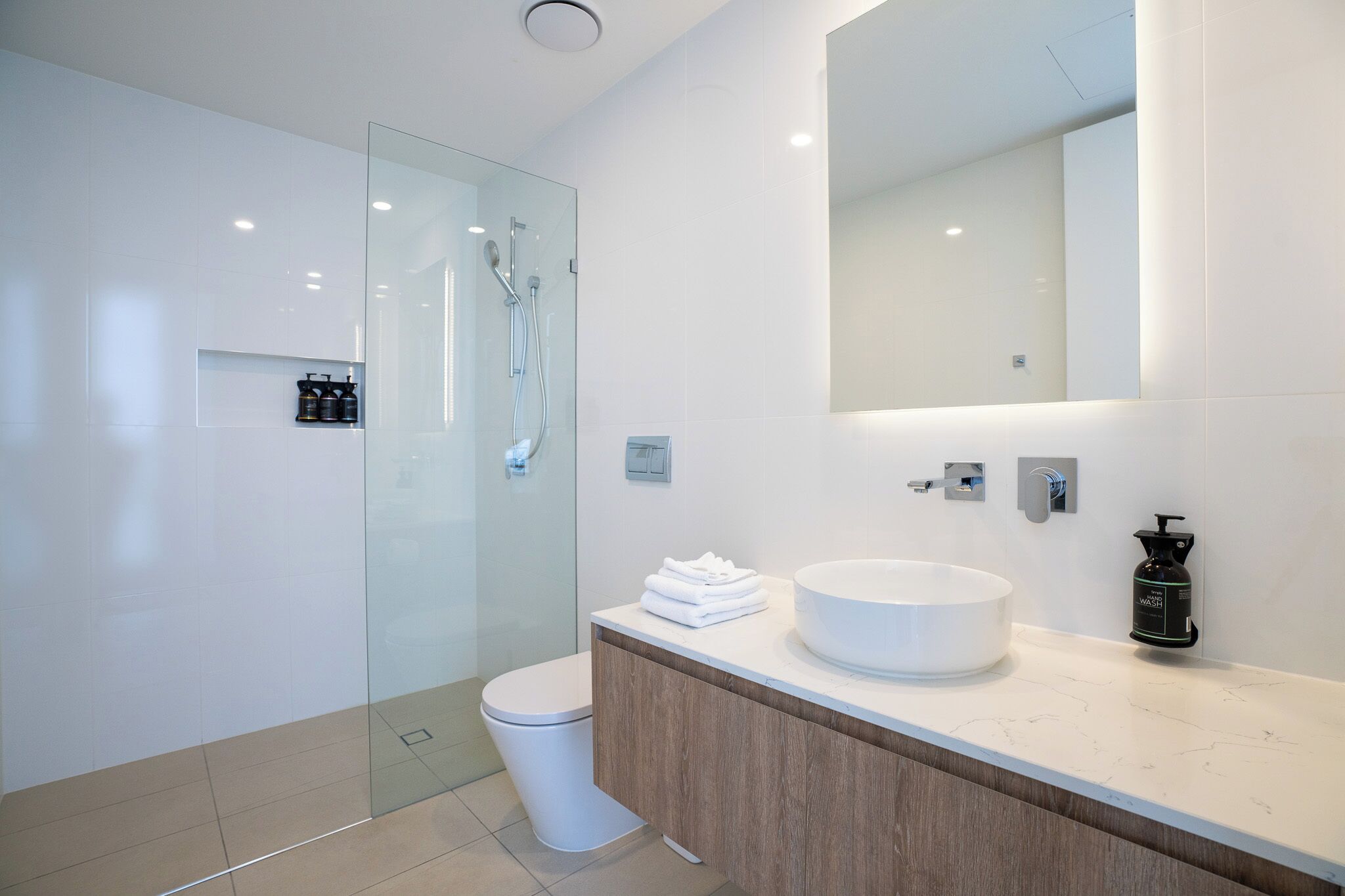 Un bagno moderno con doccia vetrata, lavabo bianco e uno specchio grande.