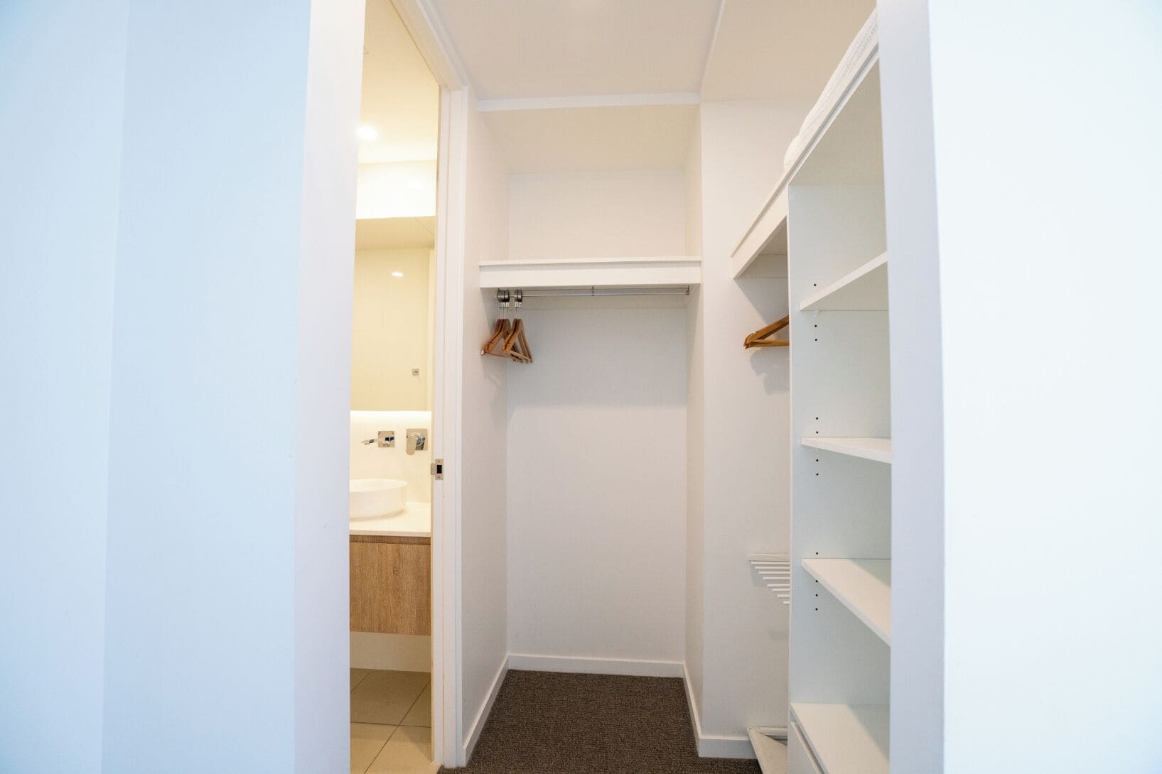 A narrow hallway with a closet on the right, a door leading to a bathroom on the left, and a coat rack above the closet.