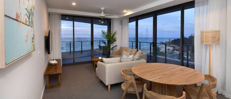 A modern living room with a large window, a round wooden table, and a sofa.