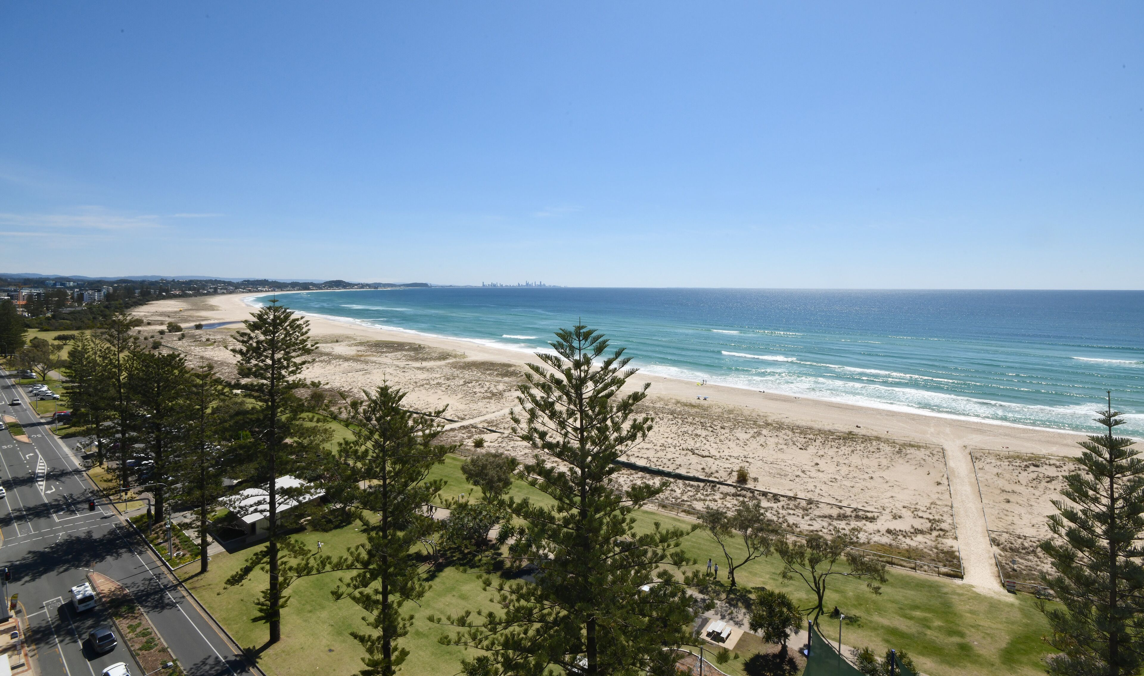 A coastal view with a beach, ocean, and a road leading to a parking area.