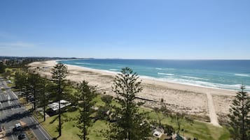 A coastal view with a beach, ocean, and a road leading to a parking area.
