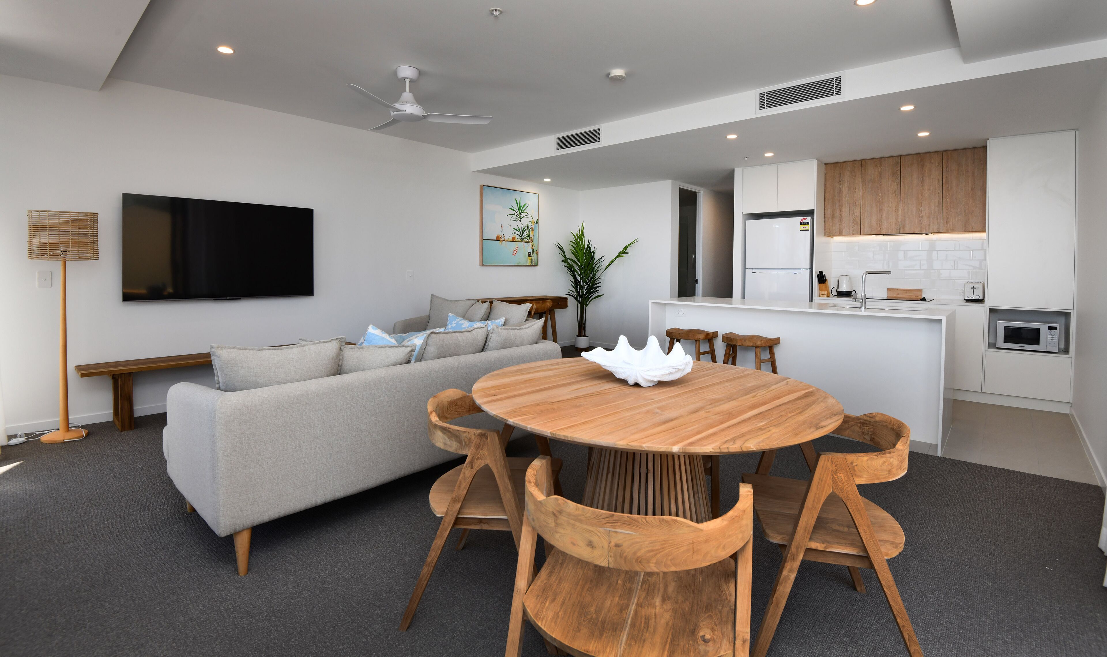 Ein modernes Wohnzimmer mit grauem Sofa, einem Holzesstisch und einer Küchenzeile.