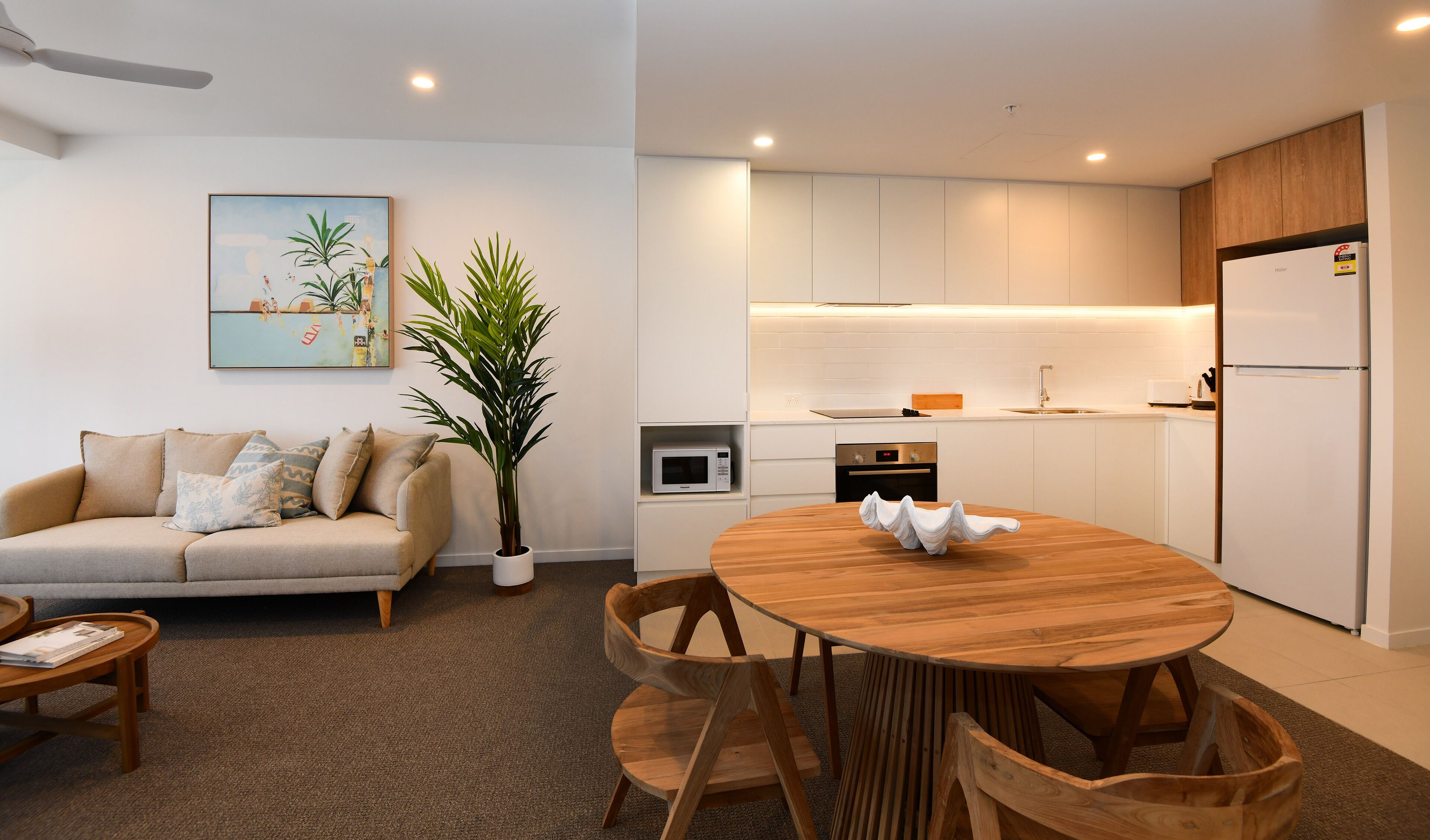 Una sala de estar moderna con un sofá, una mesa de centro y una mesa de comedor con sillas. Hay una cocina con microondas, horno y refrigerador.