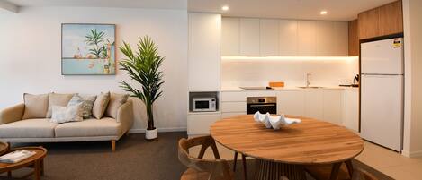 Una sala de estar moderna con un sofá, una mesa de centro y una mesa de comedor con sillas. Hay una cocina con microondas, horno y refrigerador.