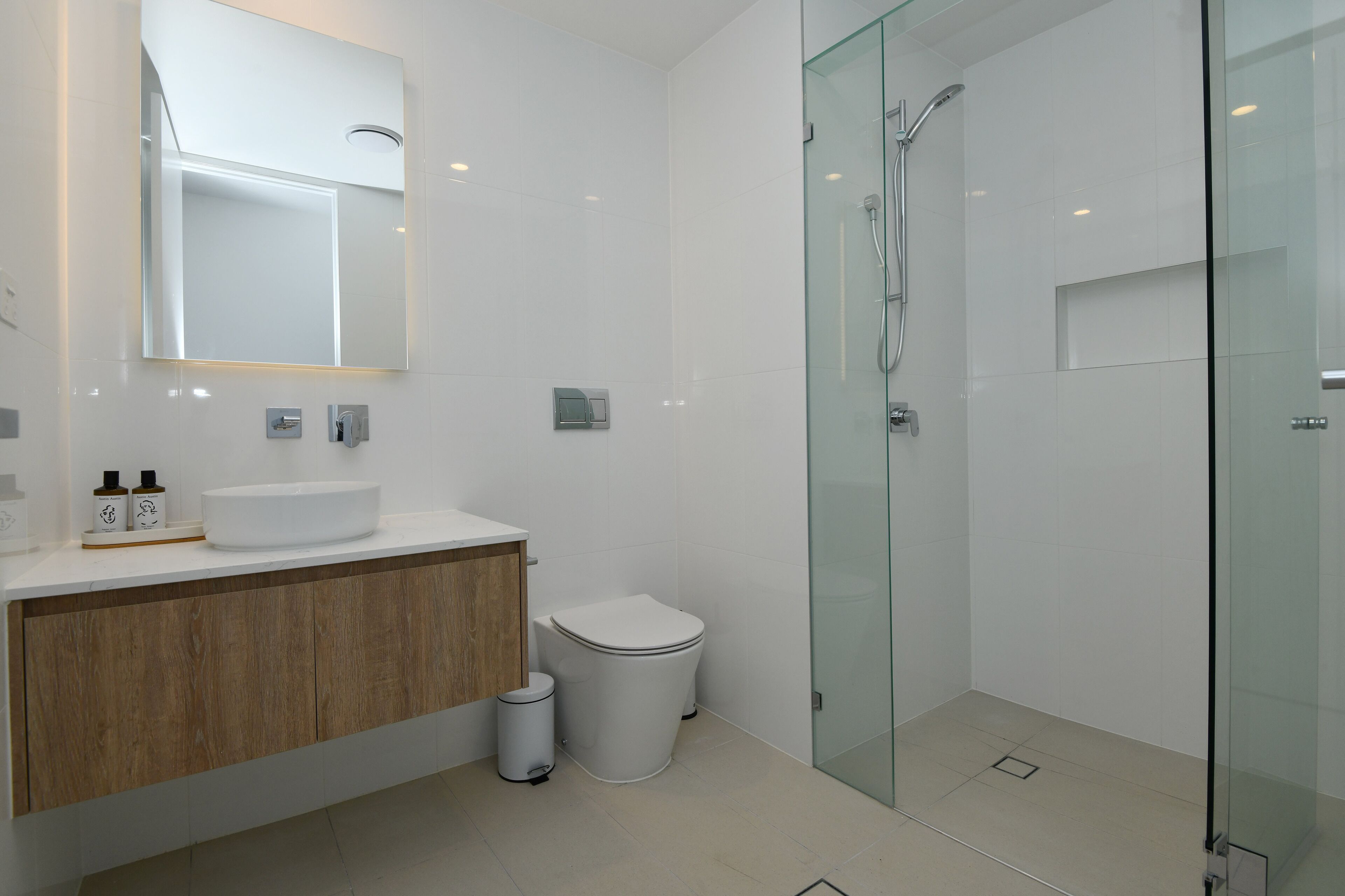 Un baño moderno con cabina de ducha de vidrio, tocador de madera y lavamanos blanco.