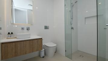 Un baño moderno con cabina de ducha de vidrio, tocador de madera y lavamanos blanco.