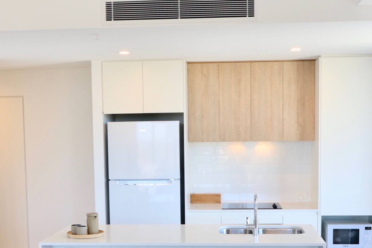 A modern kitchen with white cabinetry, a built-in refrigerator, and a round wooden dining table with chairs.