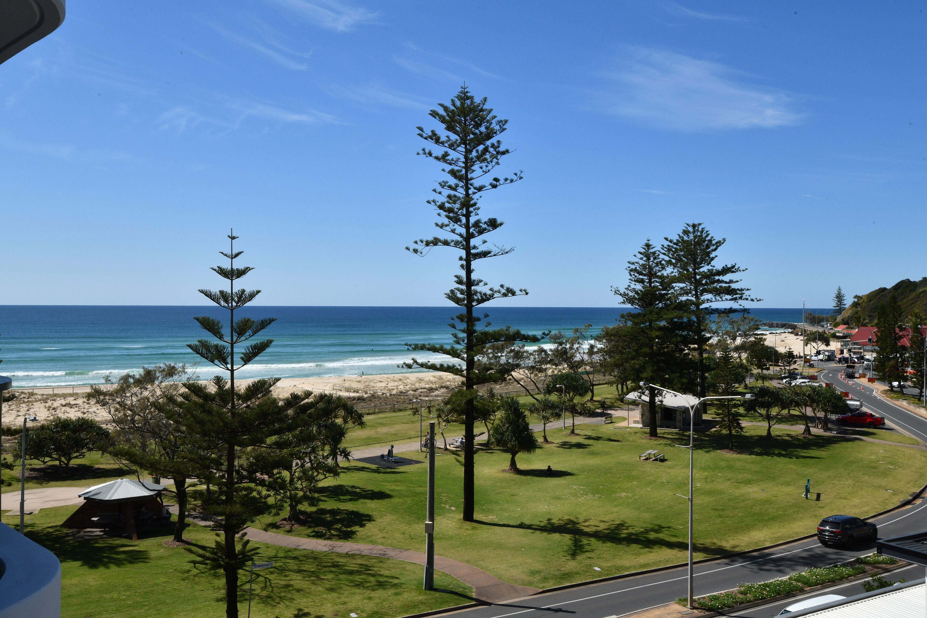 A coastal view with a beach, grassy areas, and a road with vehicles.