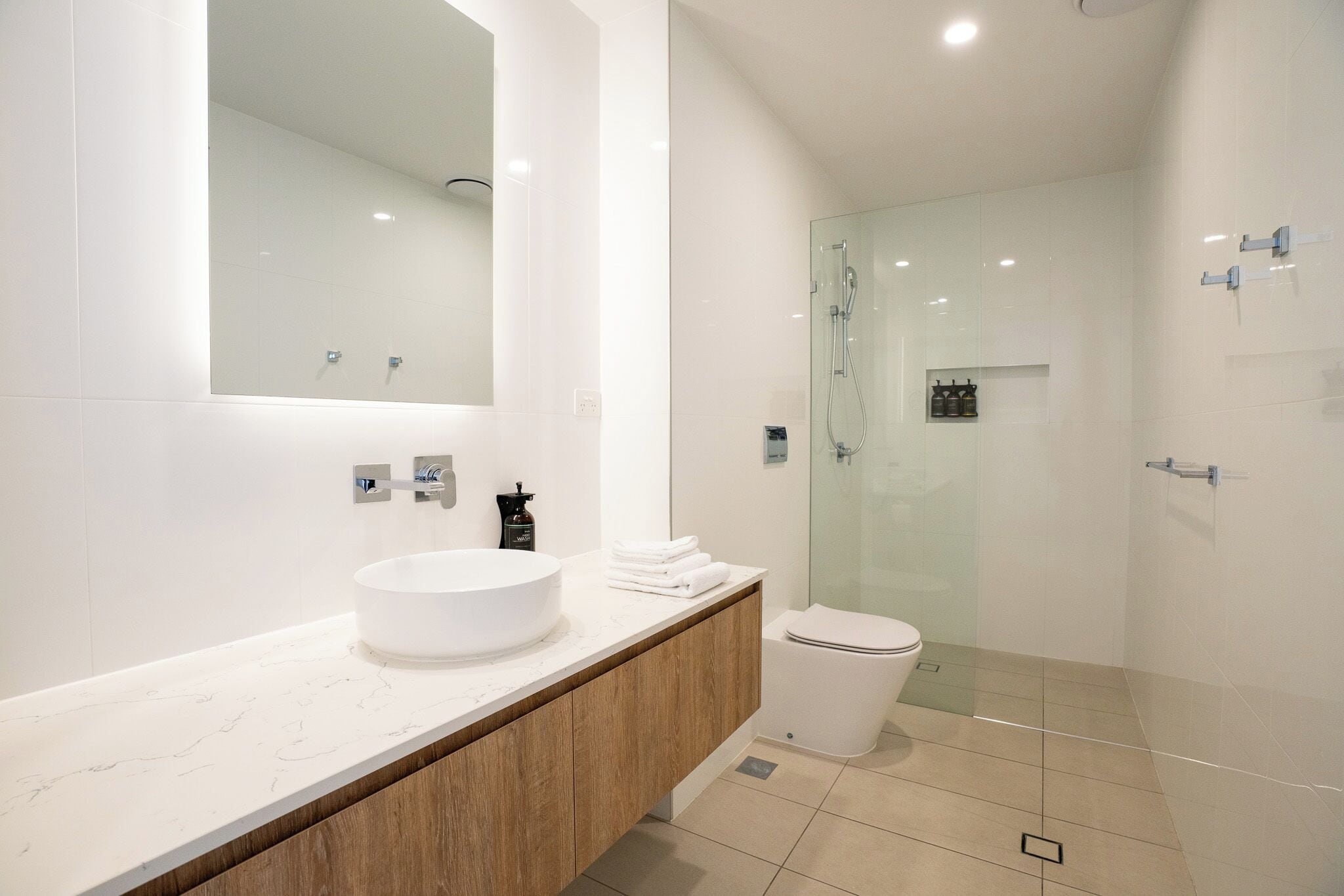Une salle de bain moderne avec un grand miroir, un lavabo blanc, des toilettes et une douche à parois de verre.