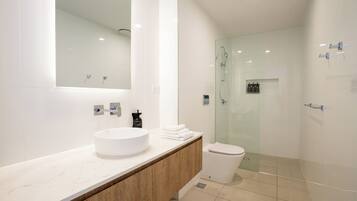 Une salle de bain moderne avec un grand miroir, un lavabo blanc, des toilettes et une douche à parois de verre.