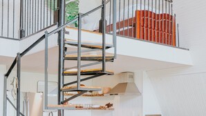 A modern kitchen with a central island, a spiral staircase, and a mezzanine level with bookshelves.