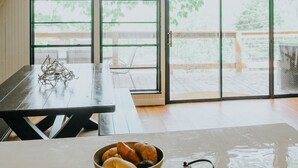 A spacious room with a high ceiling, large windows, a wooden table, and a bowl of bread on a tray.