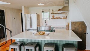 A kitchen with a large island, bar stools, a refrigerator, a sink, and a mirror above the counter.