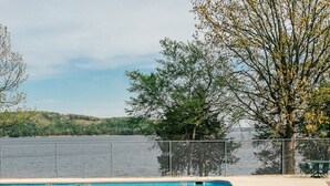 A clear blue swimming pool with a 3 ft no diving sign, surrounded by a sandy deck and a view of a lake and hills.