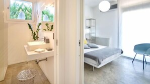 Quarto moderno com cama, mesa de cabeceira e janela com vista para o verde.