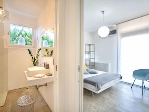 Une chambre moderne avec un lit, une table de chevet et une fenêtre donnant sur un paysage verdoyant.