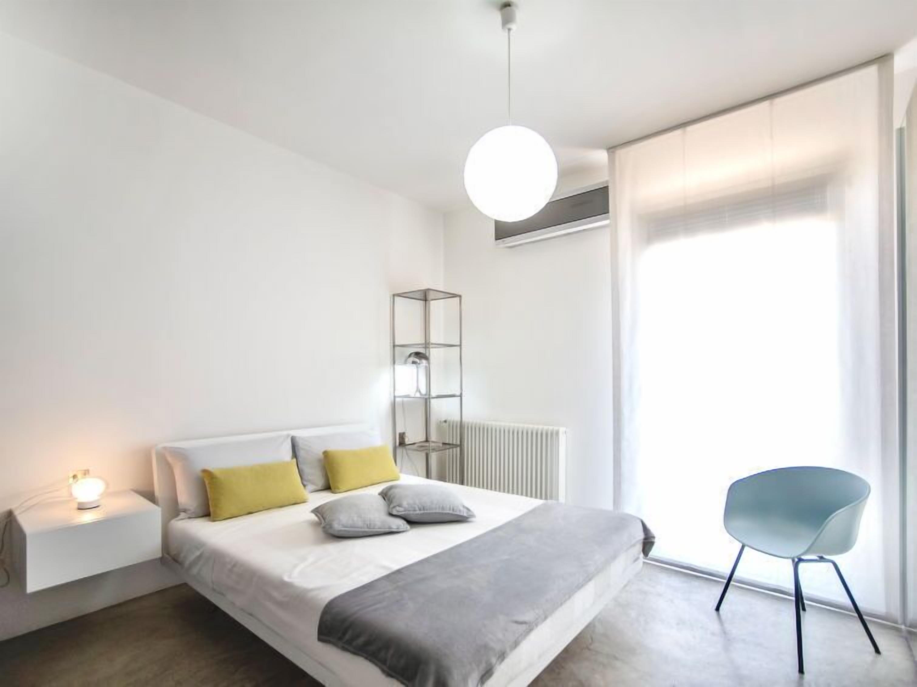 A modern bedroom with a bed, bedside table, lamp, and a chair.