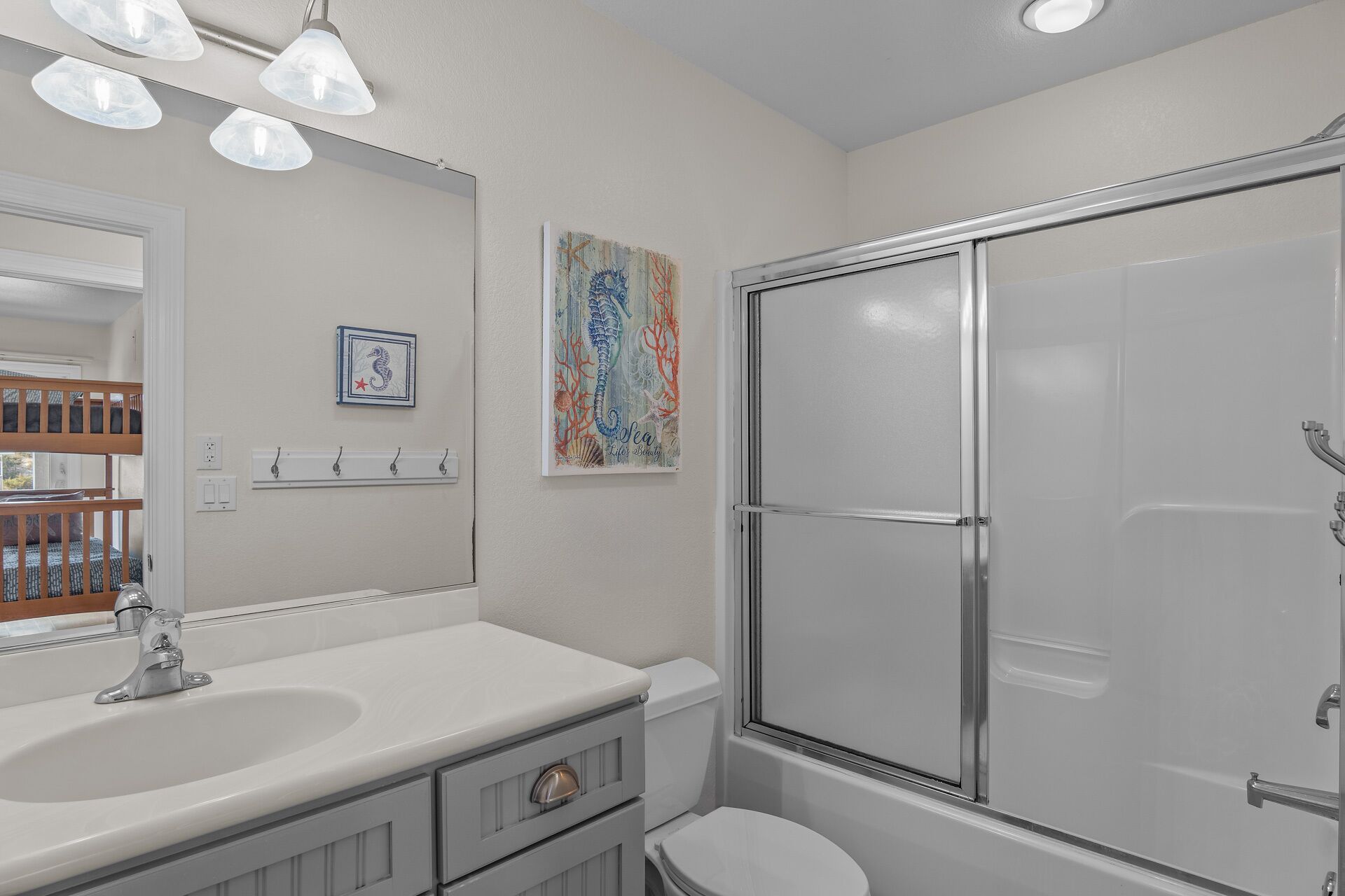 A bathroom with a shower, sink, and toilet. There is a mirror above the sink, and artwork on the wall.