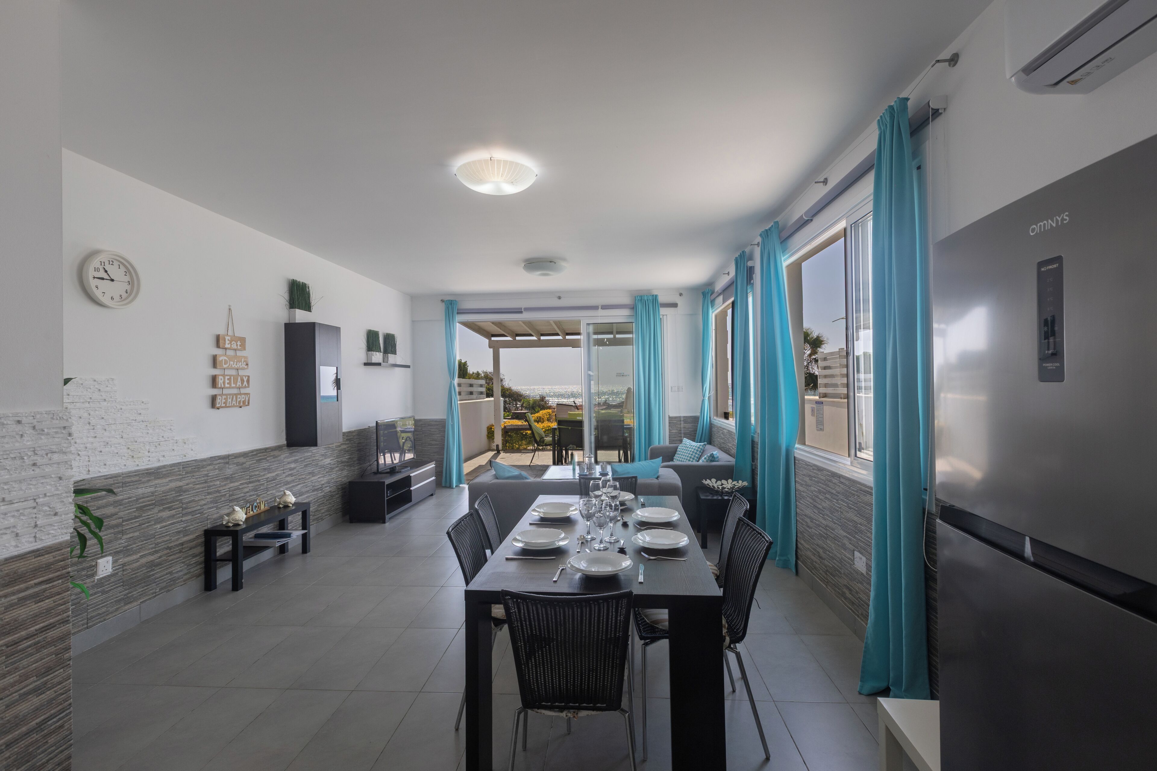 A modern dining area with a table set for four, a refrigerator, and a view of the outdoors.