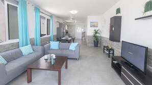 A living room with a sofa, coffee table, TV, and a dining area in the background. - Villa Suri, Luxury Seafront Villa (Sotira)