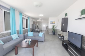 A living room with a sofa, coffee table, TV, and a dining area in the background. - Villa Suri, Luxury Seafront Villa (Sotira)