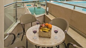 Un balcon avec des fauteuils en osier, une table avec des fruits et des verres à vin, et une vue sur l’océan.