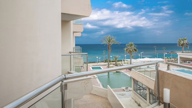 Un balcon avec une piscine, des palmiers et une vue sur l’océan.