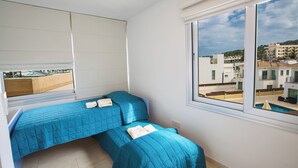 Une chambre avec deux lits, une grande fenêtre donnant sur des immeubles et un balcon.