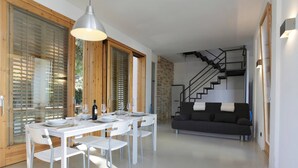 A modern interior with a dining area featuring a white table and chairs, a staircase, and a dark-colored sofa.