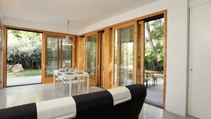 A modern room with a dining area, large sliding glass doors leading to an outdoor patio, and a black sofa with a white throw.