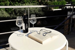 Una mesa blanca redonda con una botella de vino, dos copas y un libro con gafas encima.
